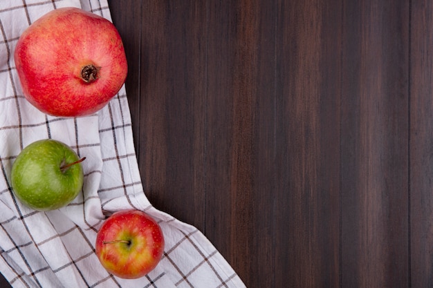 Bovenaanzicht van granaatappel met appels op een witte geruite handdoek op een houten oppervlak