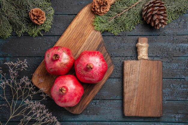 Bovenaanzicht van granaatappels en bordgranaatappels op keukenbord naast snijplank en spruce-takken met kegels
