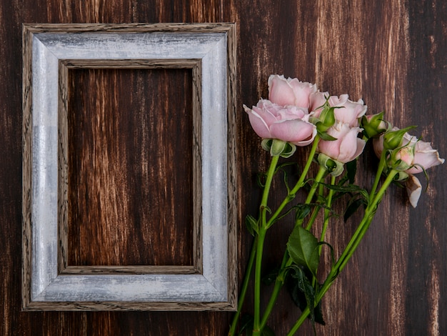 Bovenaanzicht van grijs frame met roze rozen op een houten oppervlak