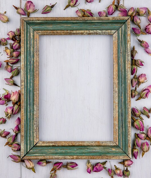 Bovenaanzicht van groenachtig gouden frame met gedroogde paarse rosebuds op een wit oppervlak