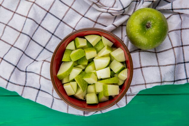 Bovenaanzicht van groene appel met gehakte plakjes op een rode kom op doek oppervlak