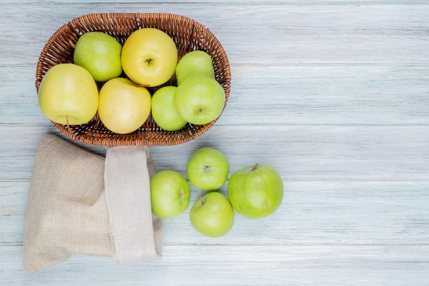 Bovenaanzicht van groene appels morsen uit zak en mand met appels op houten tafel met kopie ruimte