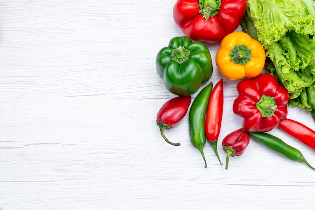 bovenaanzicht van groene salade samen met paprika en pittige paprika op wit bureau, plantaardige voedselmaaltijd