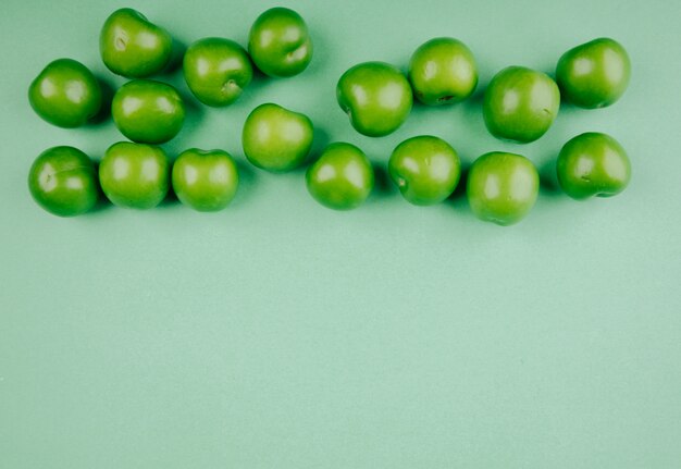 Gratis foto bovenaanzicht van groene zure pruimen geïsoleerd op groene tafel met kopie ruimte