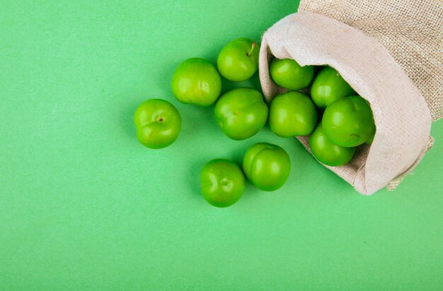 Bovenaanzicht van groene zure pruimen verspreid uit een zak op groene tafel