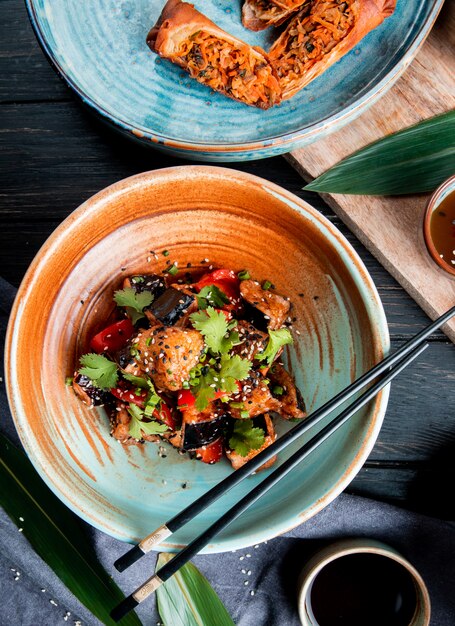 Bovenaanzicht van groente salade met gebakken aubergines tomaten kruiden en sesam in een kom geserveerd met sojasaus op hout