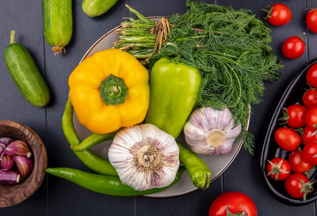 Bovenaanzicht van groenten als knoflook peper dille in plaat met knoflook kruidnagel komkommers en tomaten op zwarte ondergrond