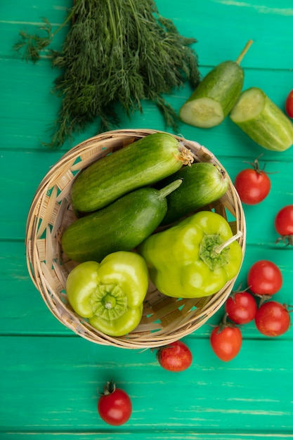 Bovenaanzicht van groenten als komkommer en peper in kom met tomatendille rond op groene ondergrond