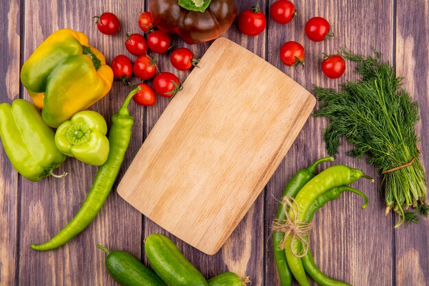 Bovenaanzicht van groenten als peper bos van komkommer dille tomaat rond snijplank op houten oppervlak