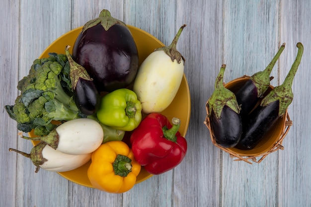 Bovenaanzicht van groenten als peper, broccoli en aubergine in plaat en aubergines in mand op houten achtergrond