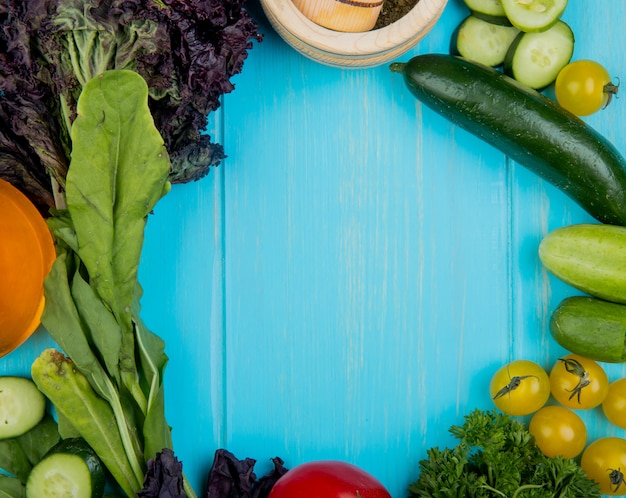 Bovenaanzicht van groenten als spinazie basilicum komkommer tomaten koriander met knoflook crusher op blauw met kopie ruimte