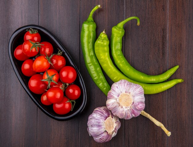 Bovenaanzicht van groenten als tomaten in kom en knoflook peper op houten oppervlak