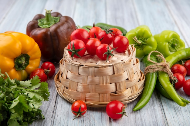 Bovenaanzicht van groenten als tomaten op mand met koriander pepers en tomaten rond op houten oppervlak