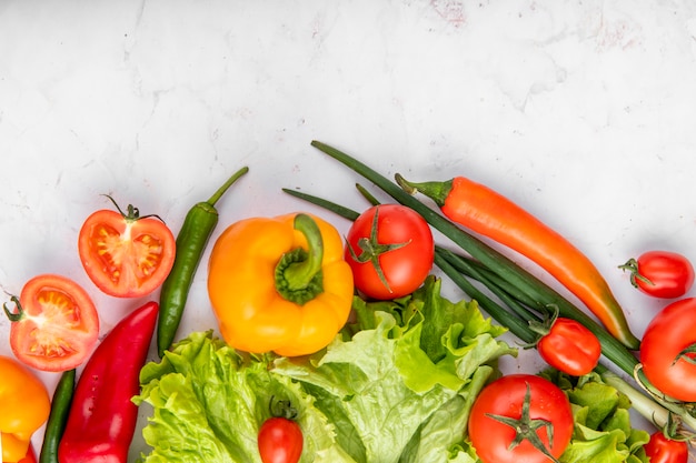 Bovenaanzicht van groenten als tomaten, paprika's, broccoli en lente-uitjes op witte ondergrond