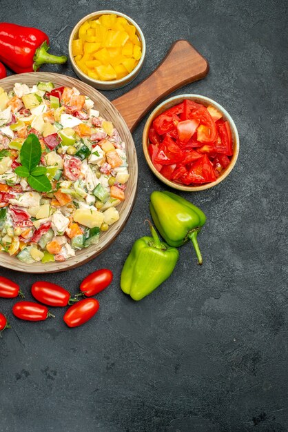 Bovenaanzicht van groentesalade met bestek en groenten aan de zijkant met vrije plaats voor uw tekst rechtsonder op donkergrijze achtergrond