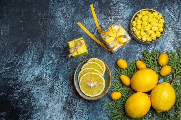 Bovenaanzicht van halve en hele verse citrusvruchten snoepjes in een pot en gele geschenkdozen op donkere achtergrond