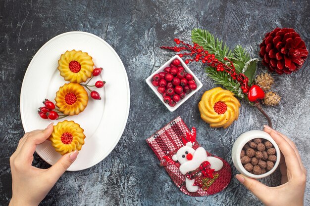 Bovenaanzicht van hand met heerlijke koekjes decoratie accessoire kerstman sok en cornell in een kom dennentakken op donkere ondergrond