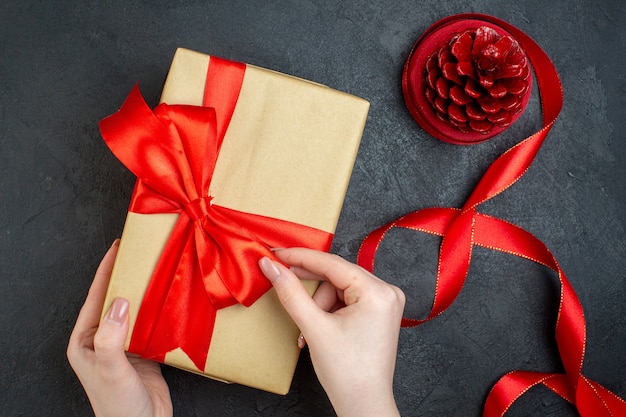 Bovenaanzicht van hand met mooi geschenk en conifer kegel op donkere achtergrond