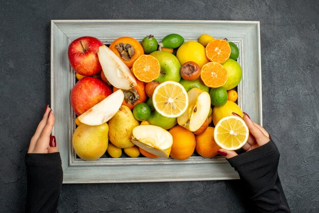 Bovenaanzicht van hand met verzameling van geheel en gesneden vers fruit in afbeeldingsframe op zwarte tafel