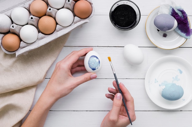 Bovenaanzicht van handen schilderij ei voor Pasen met karton en kleurstof