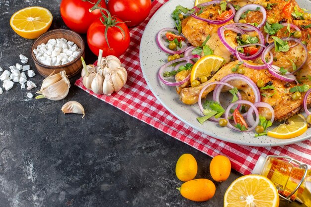Bovenaanzicht van heerlijk diner gebakken kipschotel met verschillende kruiden en voedsel tomaten met stengels knoflook gevallen oliefles aan de linkerkant op donkere kleur achtergrond