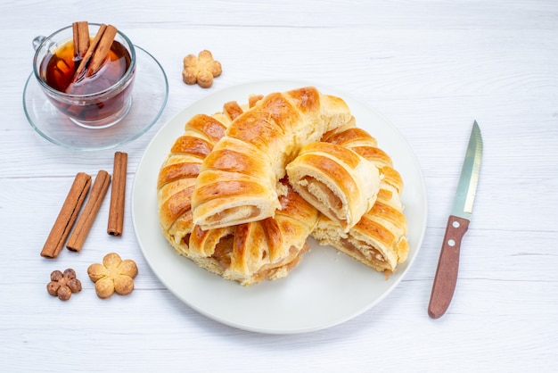 bovenaanzicht van heerlijk gebakken gebak met zoete vulling gesneden en geheel samen met koekjes en thee op licht bureau, koekjes koekjes gebak cake thee