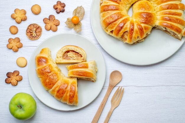 Bovenaanzicht van heerlijk gesneden gebak in plaat met vulling samen met houten vork lepel koekjes op wit bureau, gebak cookie biscuit zoete suiker