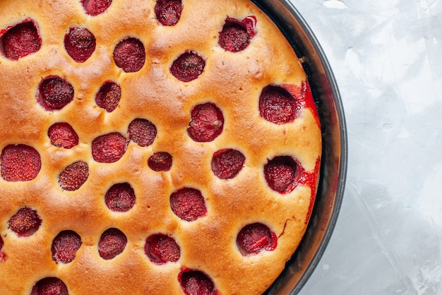 Bovenaanzicht van heerlijke aardbeientaart gebakken met verse rode aardbeien binnen met pan op licht wit bureau, cake biscuit fruit zoet deeg bakken