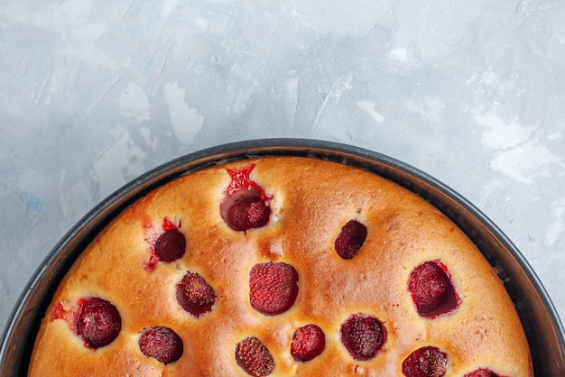 Gratis foto bovenaanzicht van heerlijke aardbeientaart gebakken met verse rode aardbeien binnen met pan op wit licht bureau, cake, koekjes, fruit, zoet, deeg, bakken