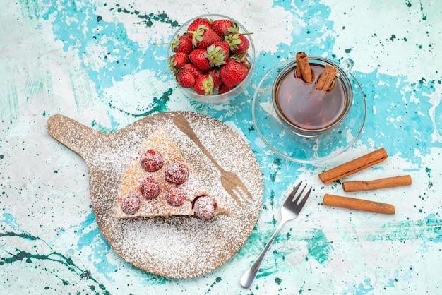 Bovenaanzicht van heerlijke aardbeientaart gesneden lekkere cake suiker gepoederd met thee op helderblauw, bessentaart zoet bakdeeg