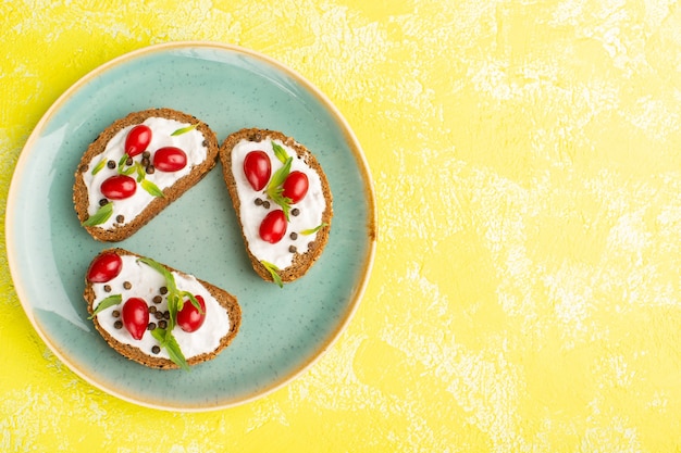 Bovenaanzicht van heerlijke brood toast met zure room en kornoeljes in blauwe plaat op het gele oppervlak