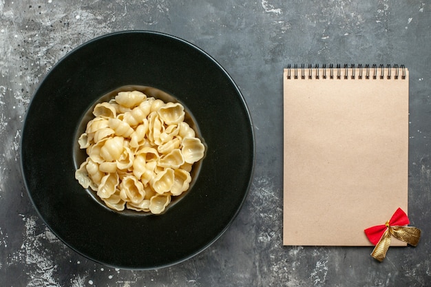 Bovenaanzicht van heerlijke conchiglie op een zwarte plaat en notitieboekje op grijze achtergrond