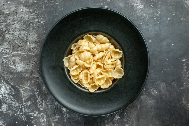 Bovenaanzicht van heerlijke conchiglie op een zwarte plaat op grijze achtergrond