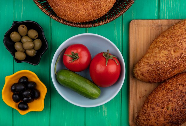 Bovenaanzicht van heerlijke en sesampasteitjes op een houten keukenbord met tomaten en komkommer op een kom met olijven op een groene houten achtergrond