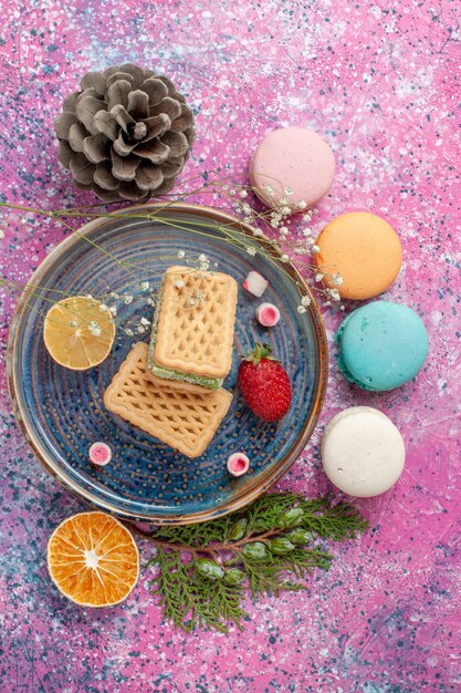 Bovenaanzicht van heerlijke Franse macarons met wafels op roze bureau