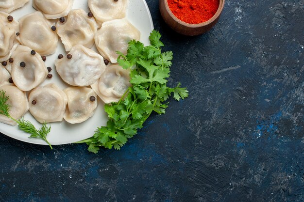 bovenaanzicht van heerlijke gebakken dumplings in plaat samen met peper en greens op donkergrijs bureau