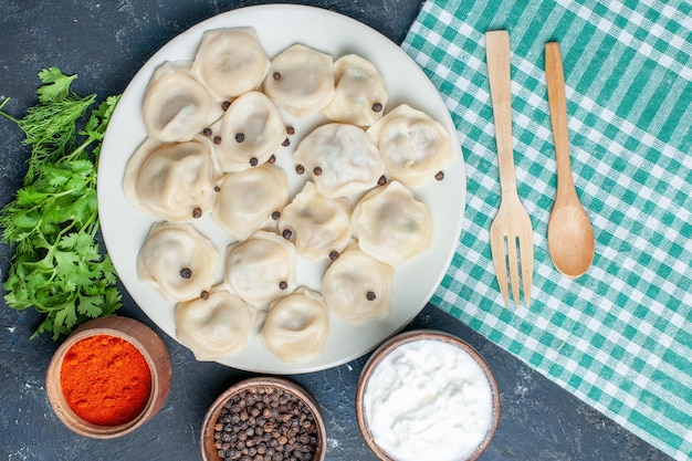Bovenaanzicht van heerlijke gebakken dumplings in plaat samen met peper-yoghurt en greens op donker bureau, deegmaaltijd diner vlees