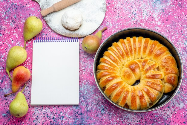 bovenaanzicht van heerlijke gebakken gebakjesarmband gevormd in de pan met blocnote en peren op helder bureau, gebakjekoekjeskoekje zoete suiker