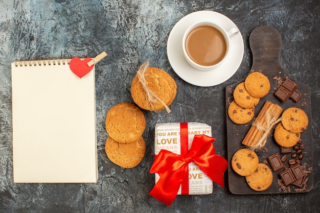 Bovenaanzicht van heerlijke koekjes, chocoladerepen en een kopje koffie spiraalvormige notebook geschenkdoos op ijzig donker oppervlak