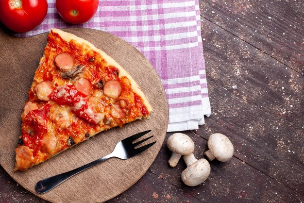 bovenaanzicht van heerlijke pizza slice met verse champignons tomaten rode paprika's op bruin bureau