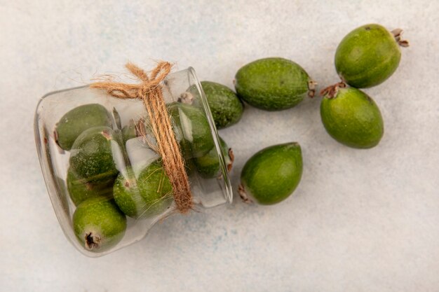 Bovenaanzicht van heerlijke rijpe feijoas die uit een glazen pot op een grijze ondergrond vallen