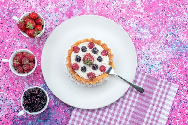 bovenaanzicht van heerlijke romige cake met verschillende verse bessen op helder licht bureau, bessenfruit vers zuur