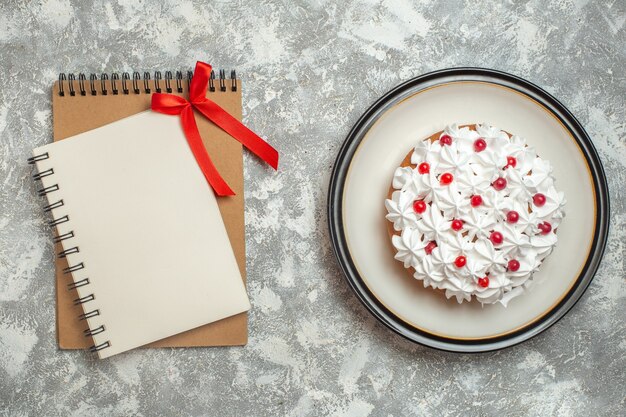 Bovenaanzicht van heerlijke romige cake versierd met fruit en notitieboekjes op ijsachtergrond