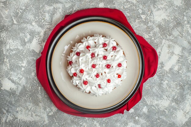 Bovenaanzicht van heerlijke romige cake versierd met fruit op een rode handdoek op ijsachtergrond