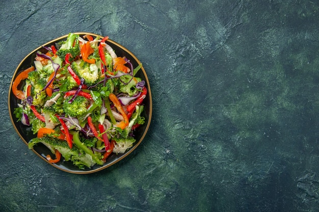 Bovenaanzicht van heerlijke veganistische salade in een bord met verschillende verse groenten aan de rechterkant op donkere achtergrond