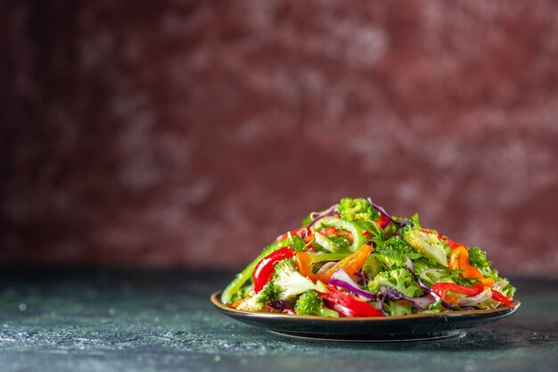 Bovenaanzicht van heerlijke veganistische salade met verse ingrediënten in een bord aan de linkerkant op blauwe en kastanjebruine wazige achtergrond