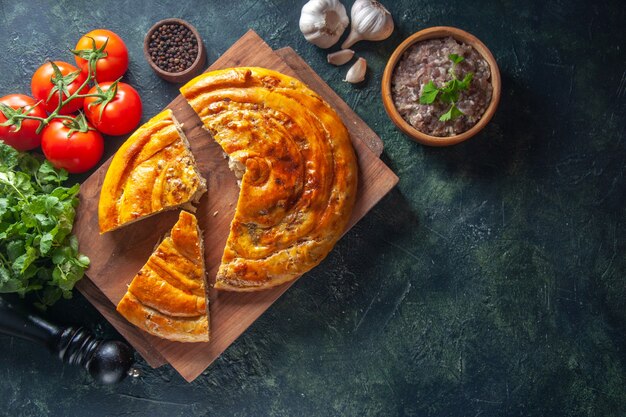 Bovenaanzicht van heerlijke vleespastei met ingrediënten op donkere ondergrond