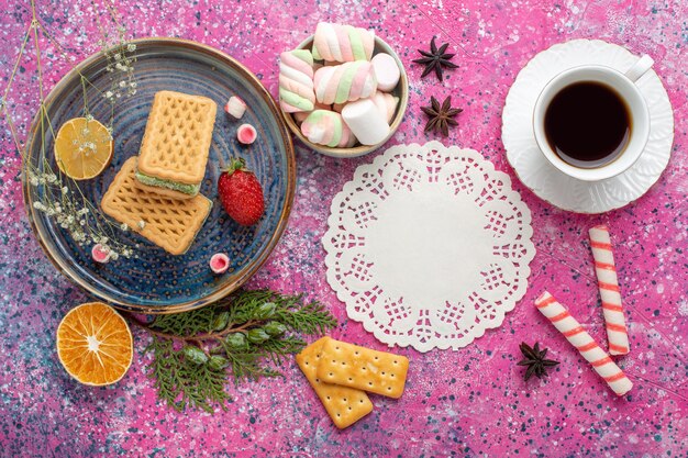 Bovenaanzicht van heerlijke wafels met kopje thee en marshmallow op het lichtroze oppervlak