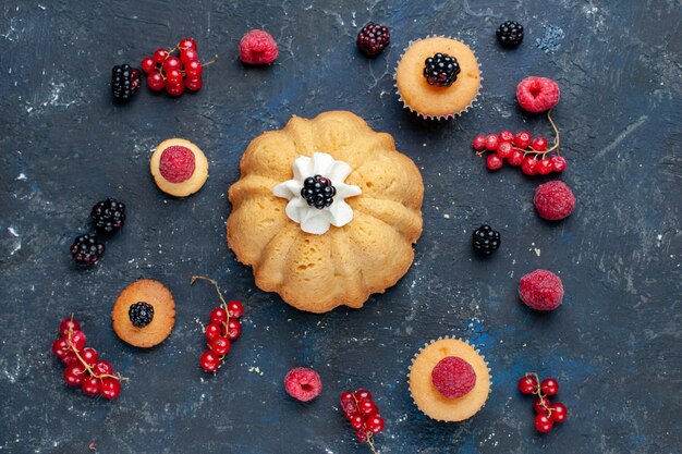 Bovenaanzicht van heerlijke zoete cake met verschillende bessen en lekkere room samen met veenbessen verspreid op een donker bureau, zoete fruitbessentaart