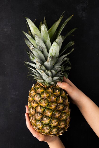 Bovenaanzicht van hele ananas vastgehouden door vrouwenhanden op zwarte ondergrond